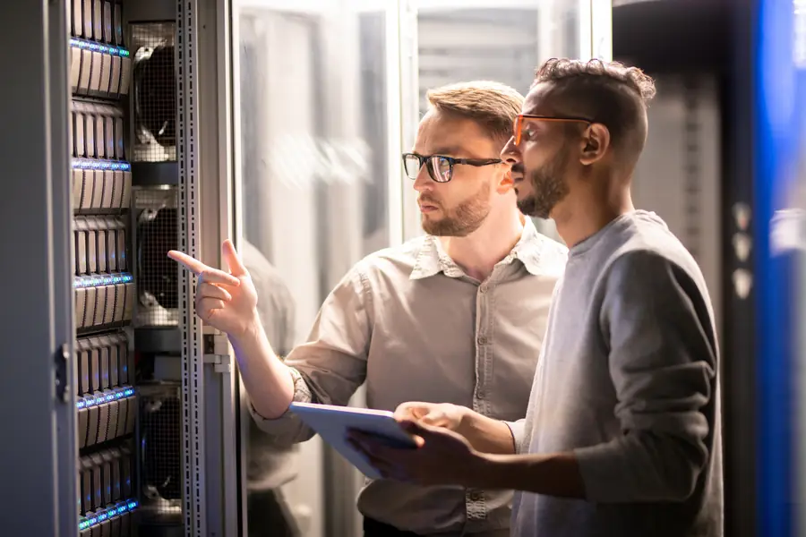 Two engineers reviewing a tablet beside server racks in a data centre
