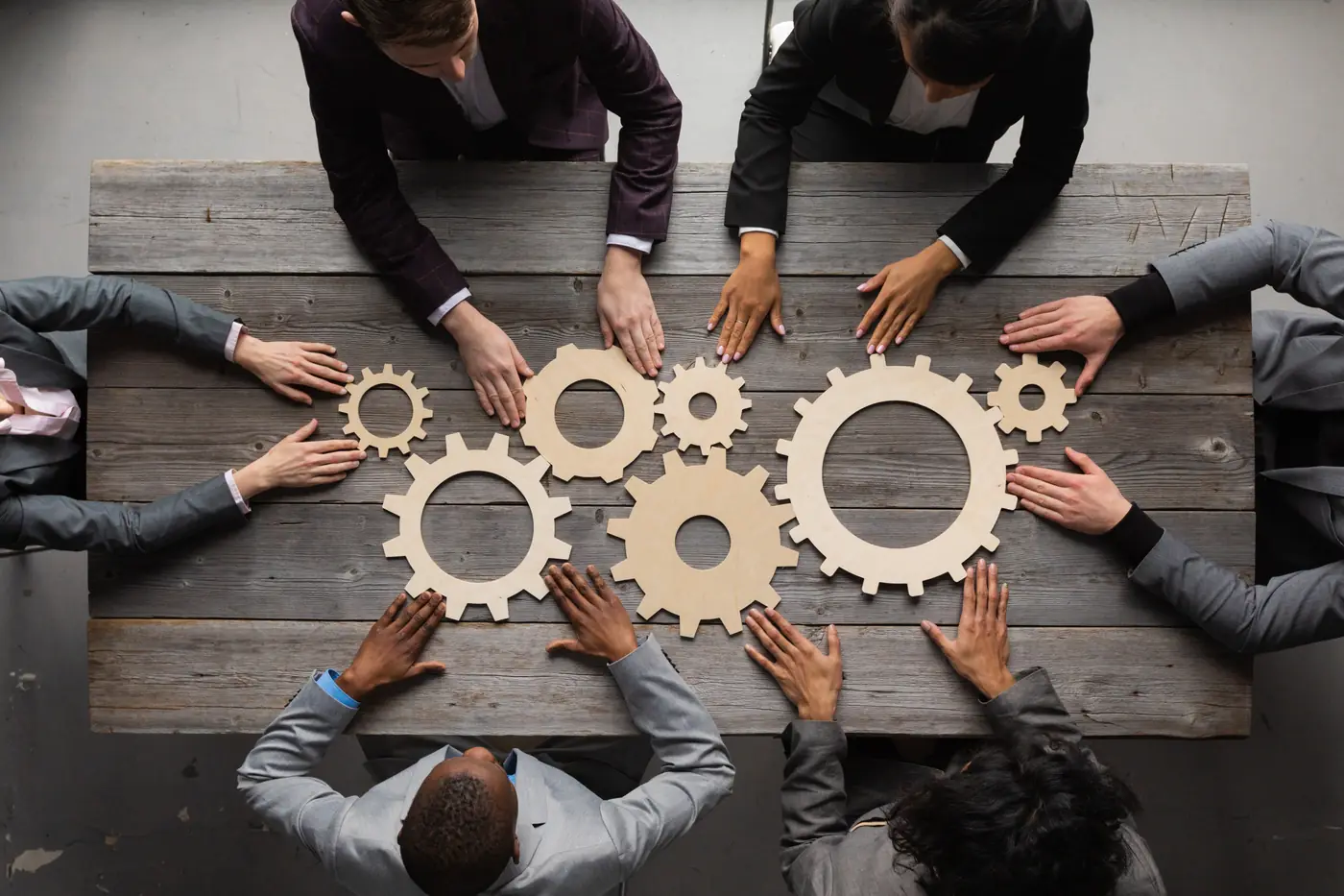 Colleagues around a table joining wooden gears together, representing teamwork
